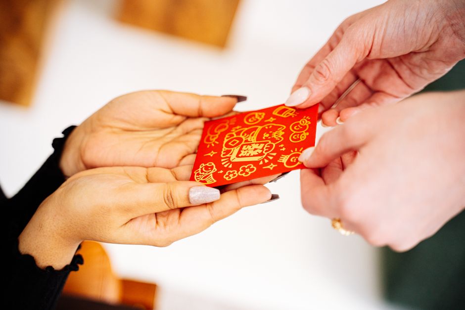 Hands exchanging a decorative red envelope for Lunar New Year, symbolizing good luck and prosperity.